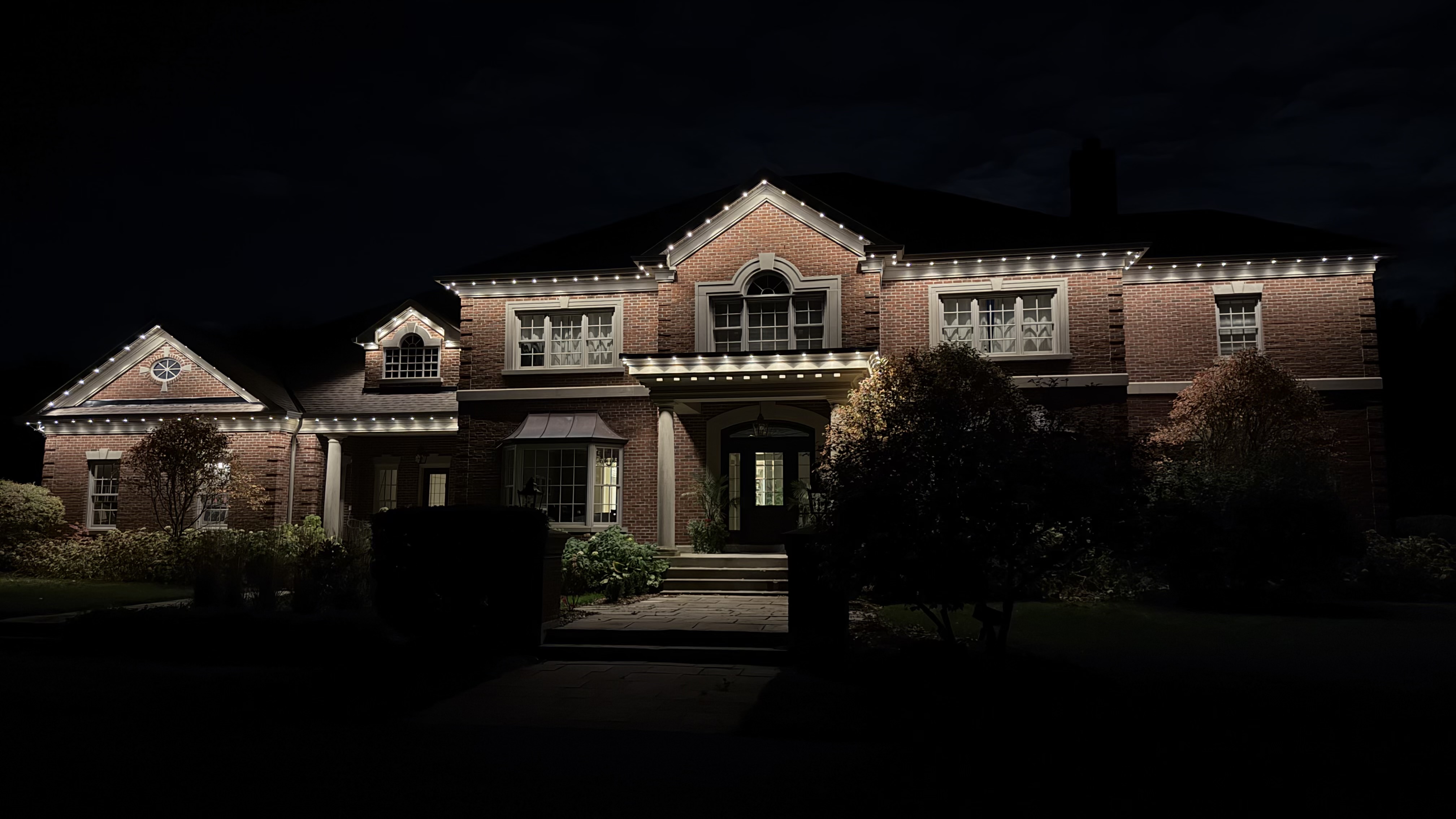 A brick estate home outlined in warm white permanent LED lighting at night