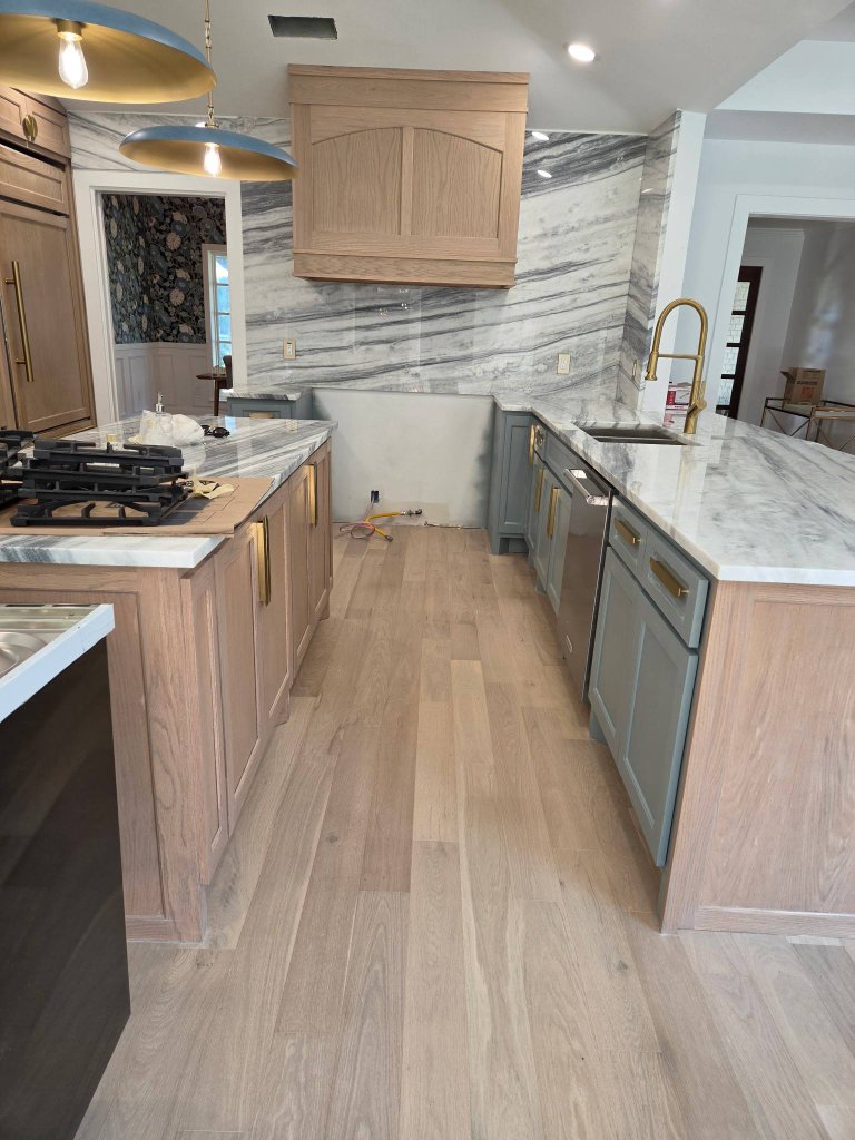 Completed residential kitchen with a natural oak island, custom wood range hood, marble surfaces, and blue-grey lower cabinetry in McKinney