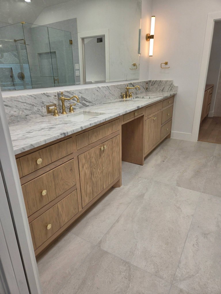 Custom white oak double vanity with marble countertop, brass faucets, and a frameless mirror in a Frisco bathroom renovation