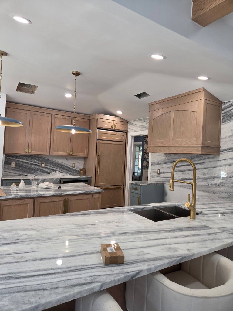 Luxury kitchen renovation with a marble island, integrated oak refrigerator panel, brass hardware, and marble backsplash in McKinney