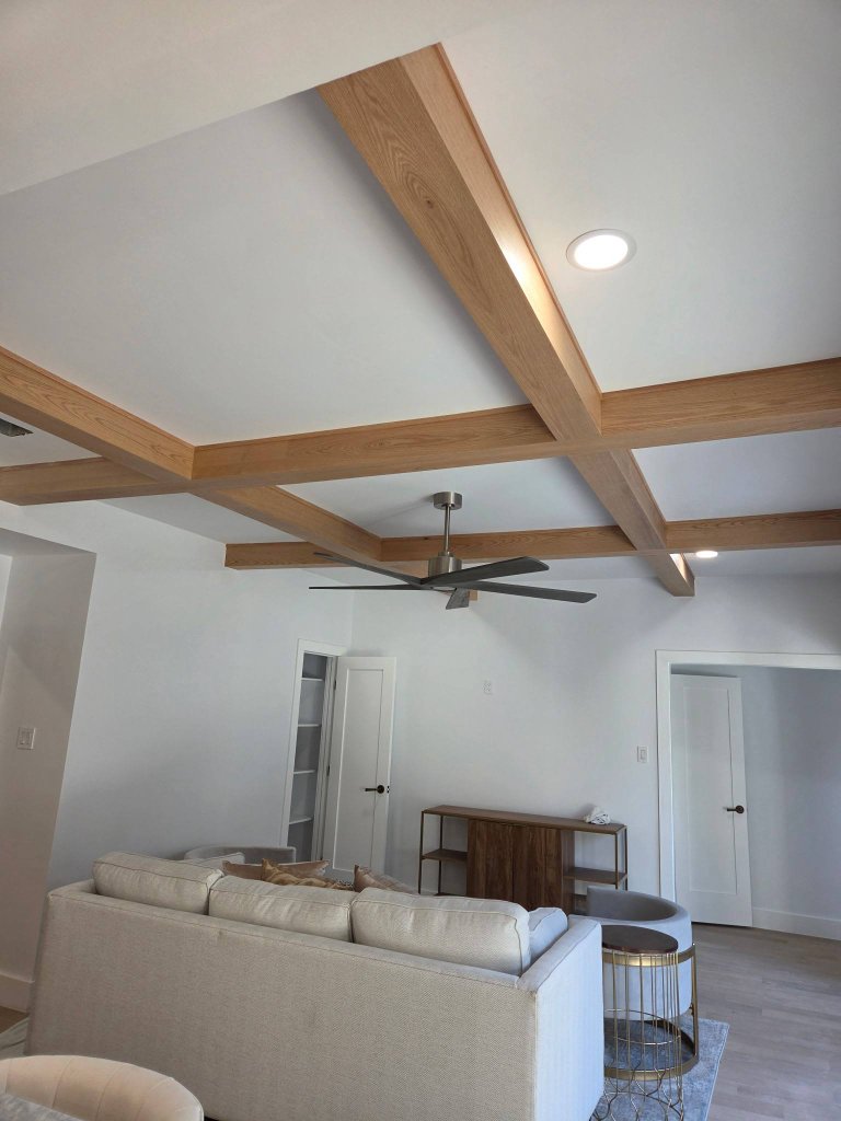 Contemporary living room with a custom coffered ceiling featuring exposed light-oak wood beams and a centered ceiling fan in a North Texas home
