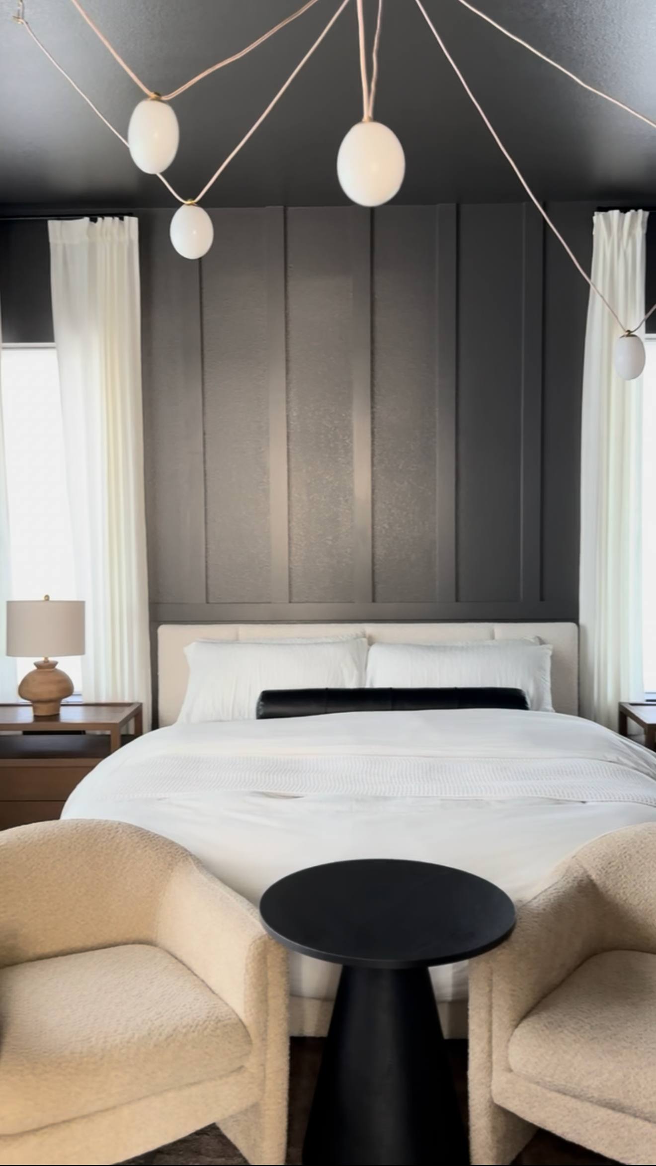 Primary bedroom with charcoal board-and-batten accent wall, beige upholstered headboard and gold chandelier