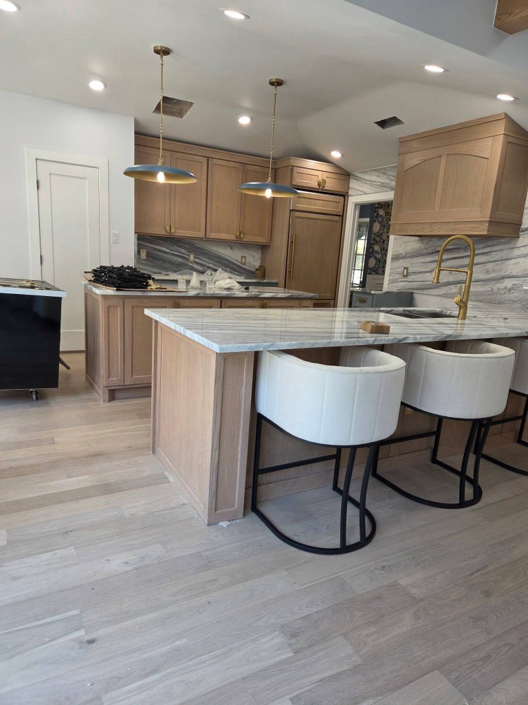 Completed modern kitchen with white oak cabinetry, a marble-topped island, custom range hood, and brass fixtures in a McKinney home