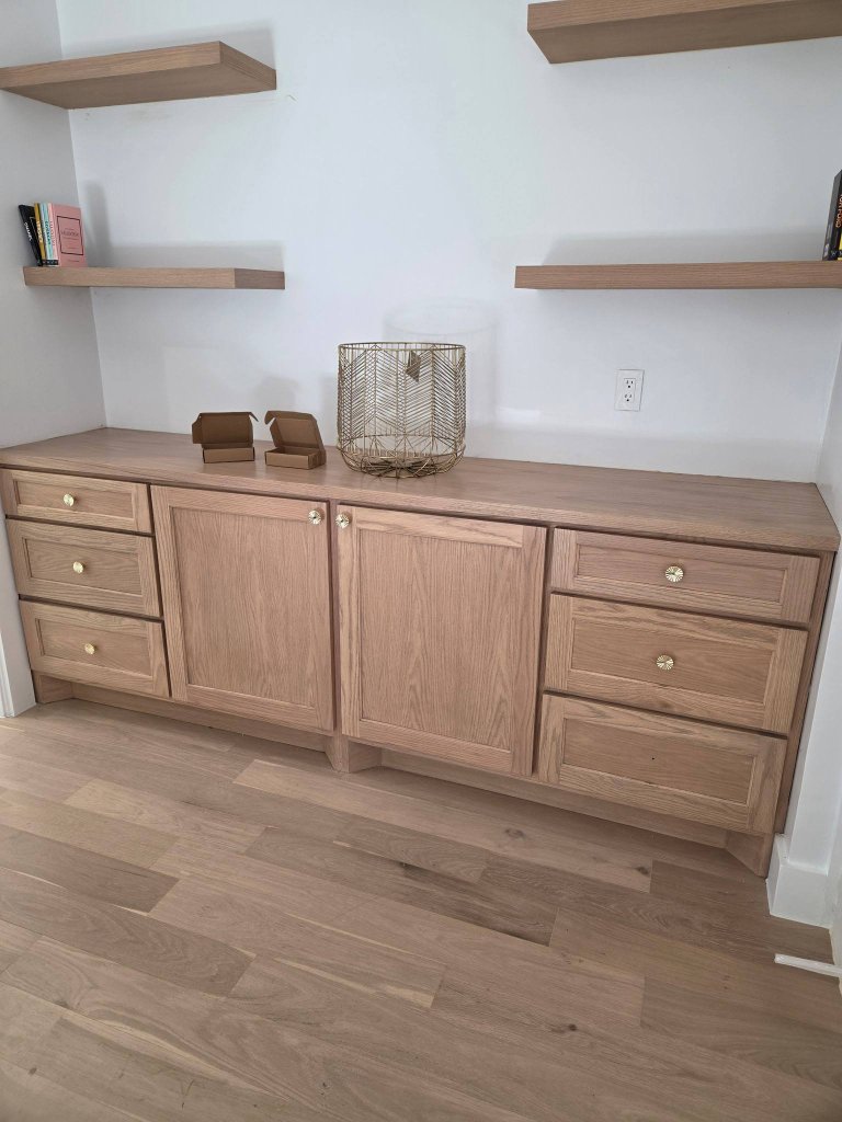 Custom light oak built-in storage cabinet with matching floating shelves and brass knobs in a Prosper home