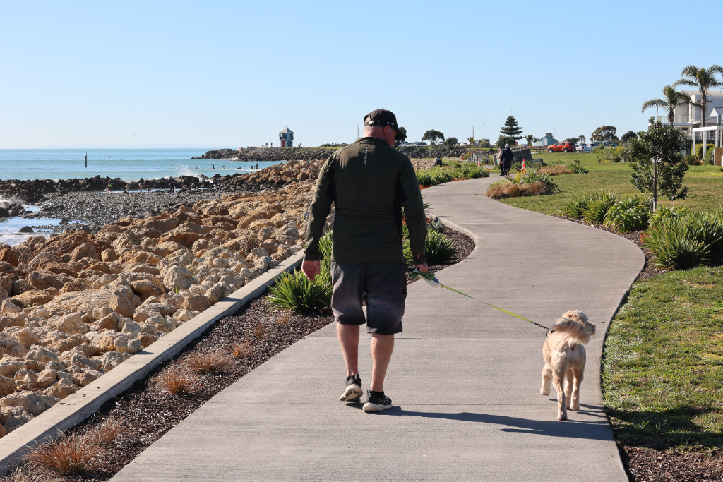 A man walking his dog along the Westshore coastal pathway
