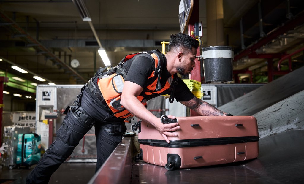 Medewerker met LiftSuit tilt bagage van lopende band
