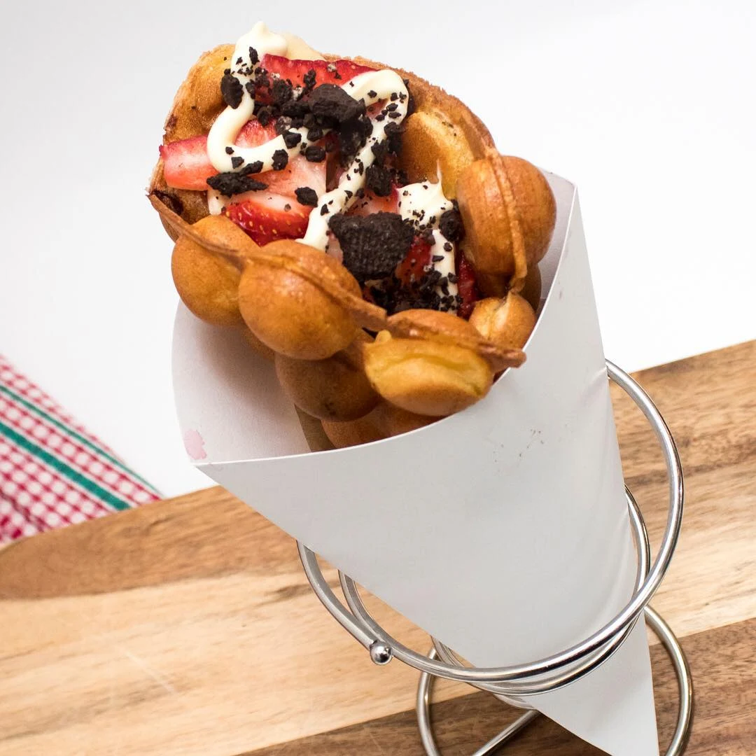 A golden Muffle topped with strawberries, crushed chocolate sandwich cookies and cheesecake drizzle
