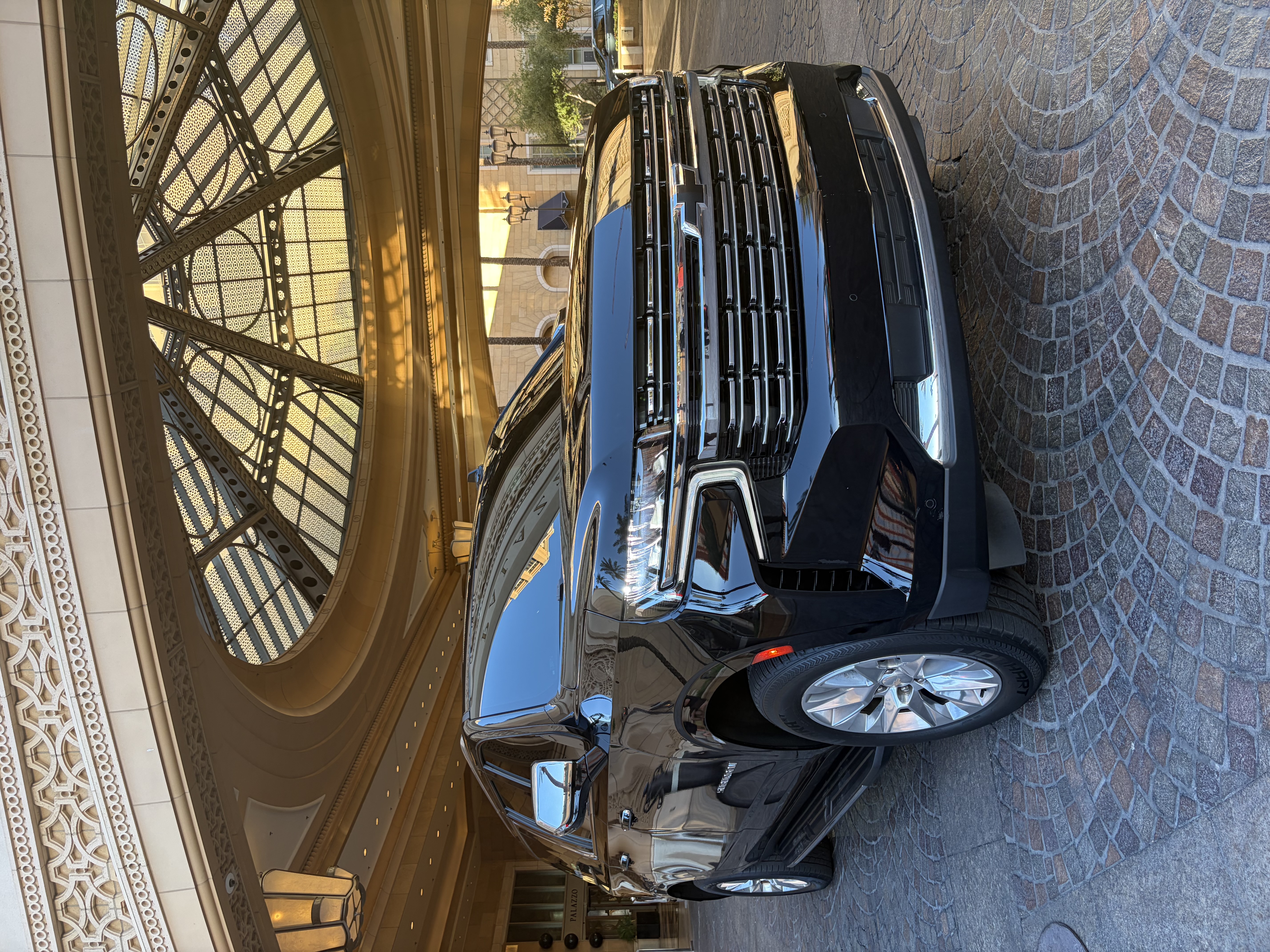 Black Cadillac Escalade front three-quarter view under a luxury hotel porte-cochère at golden hour