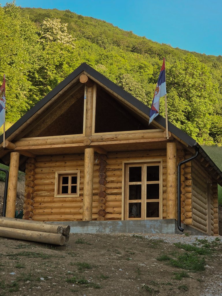 Završena brvnara — eksterijer sa krovom i zastavama