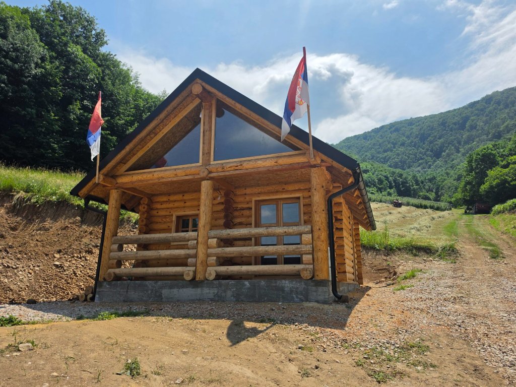 Završena brvnara — frontalni pogled sa tremom i zastavama