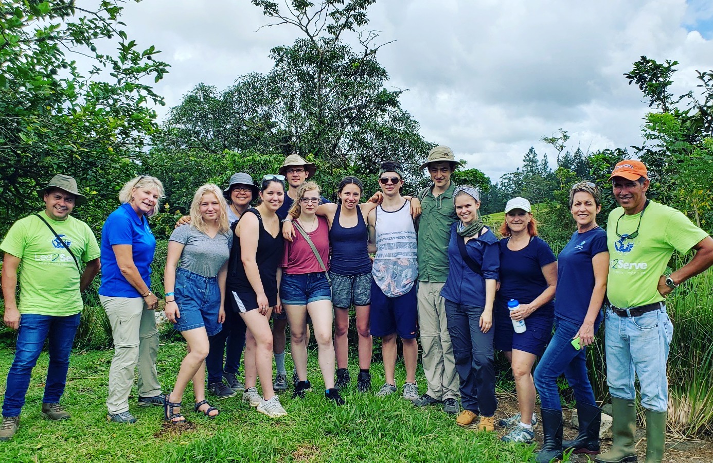 Large group of 14 volunteers standing together in a tropical setting