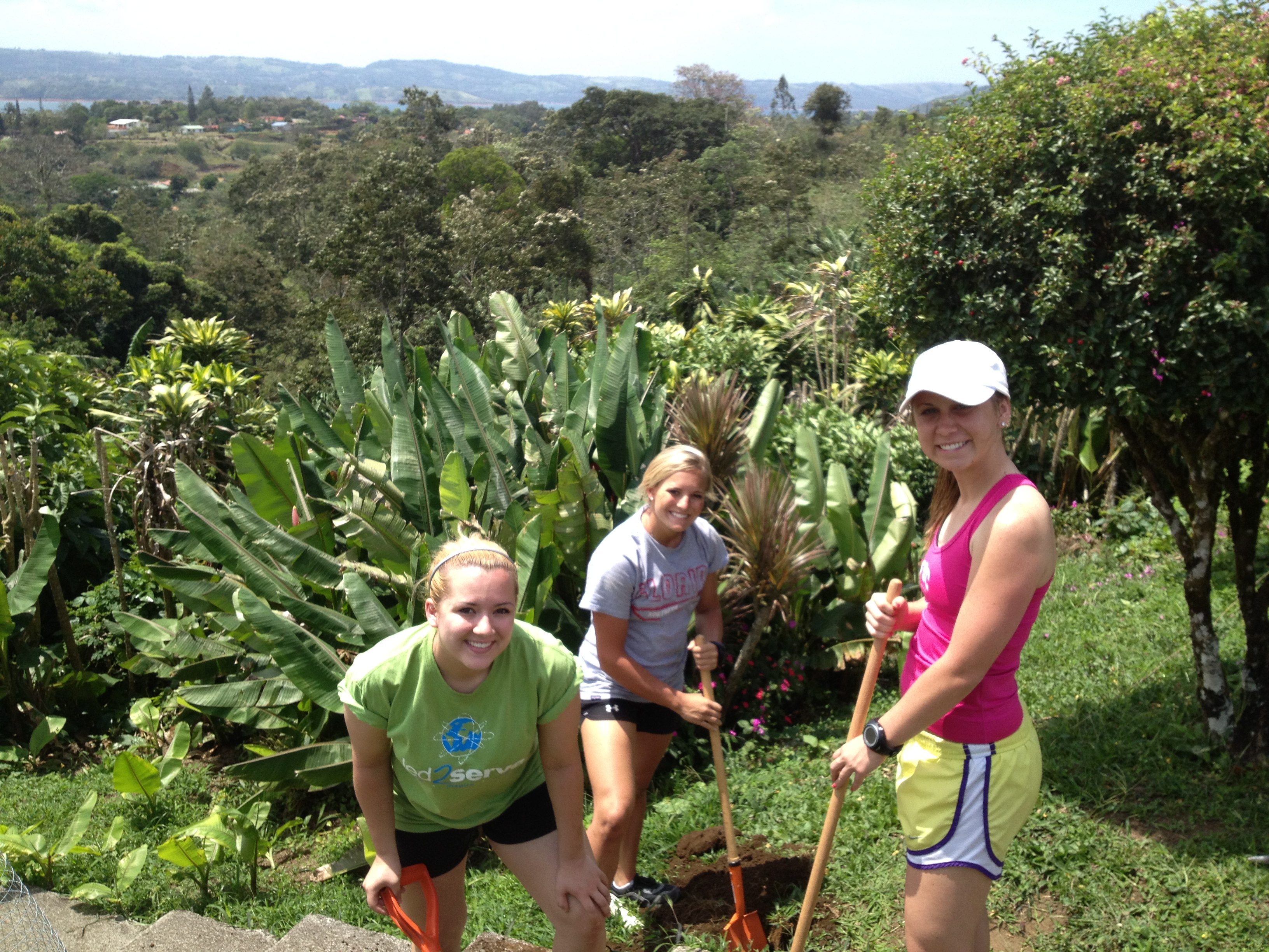 Three women volunteers digging with shovels in a grassy field