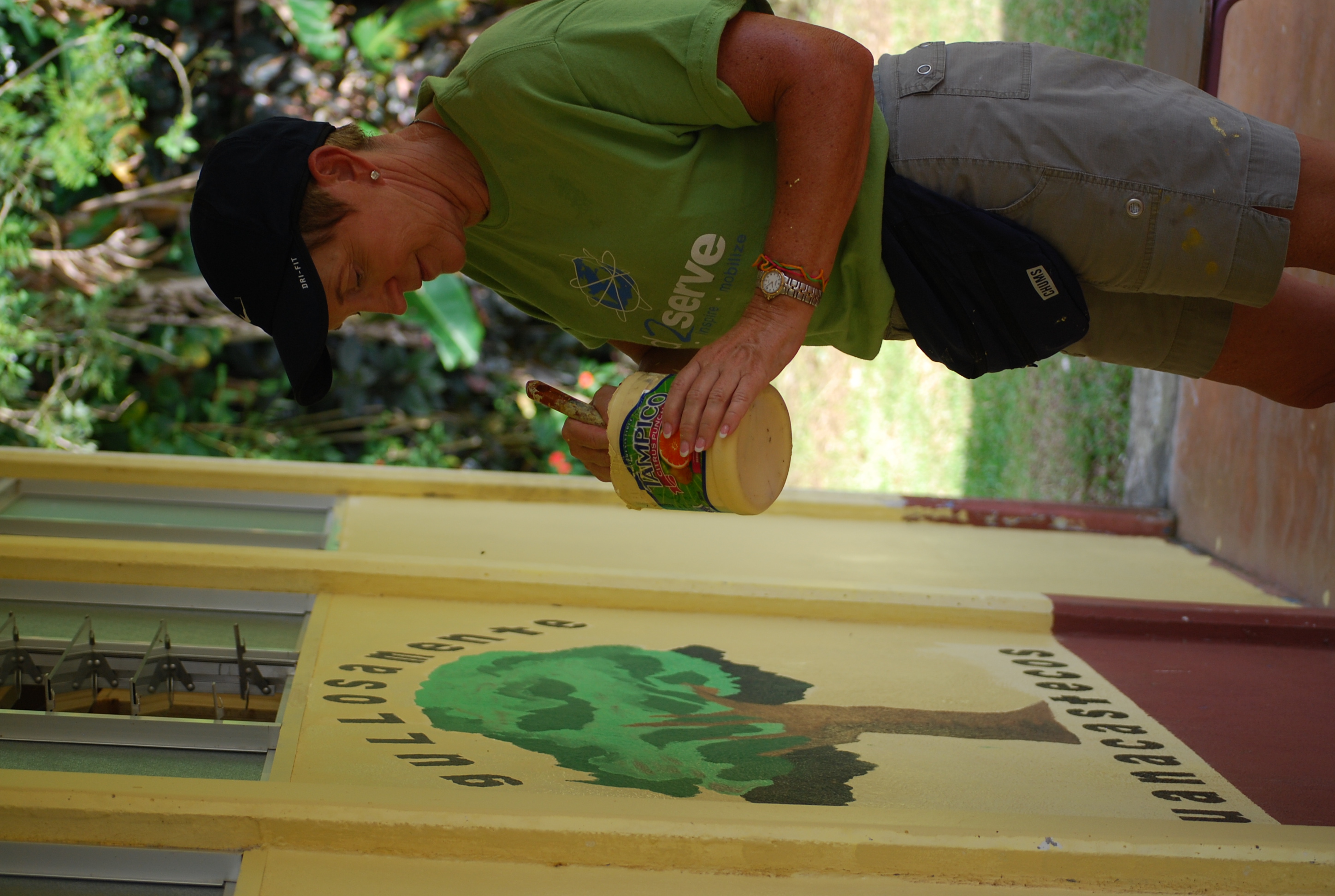 Volunteer painting a tree mural on a yellow wall