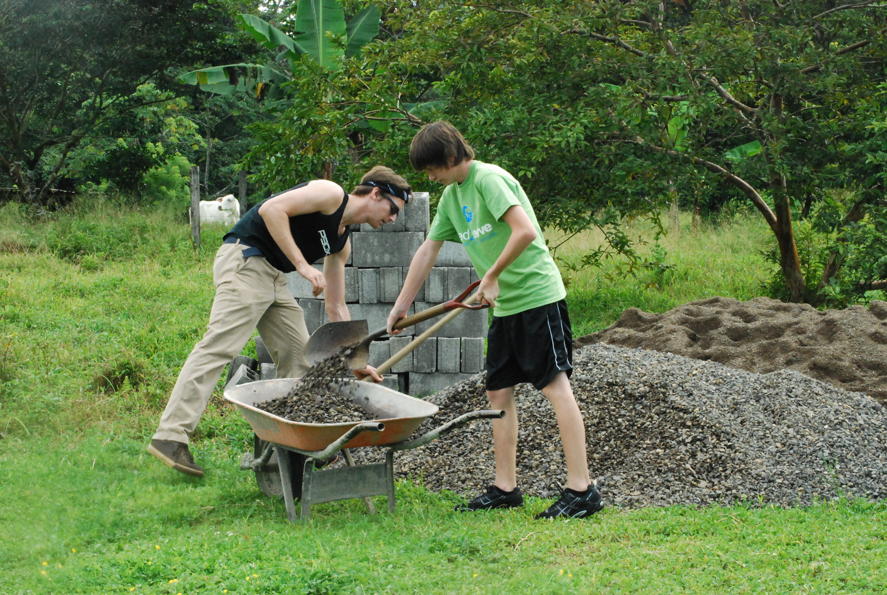 Two volunteers shoveling gravel into a wheelbarrow on a construction project