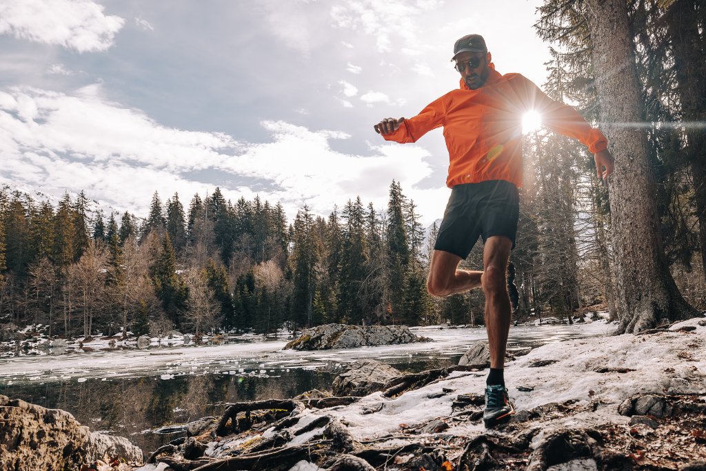 Trail runner in an orange jacket on a snowy alpine shoreline