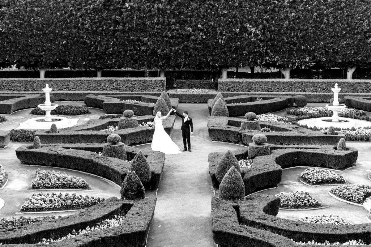 A bride and groom dancing in the centre of the formal hedge maze at Hunter Valley Gardens, stone fountains either side