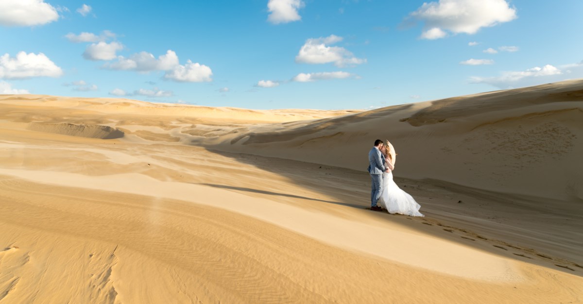 Tina and Stephen embracing on the vast Anna Bay sand dunes at Port Stephens — a real Newcastle wedding photographer feature