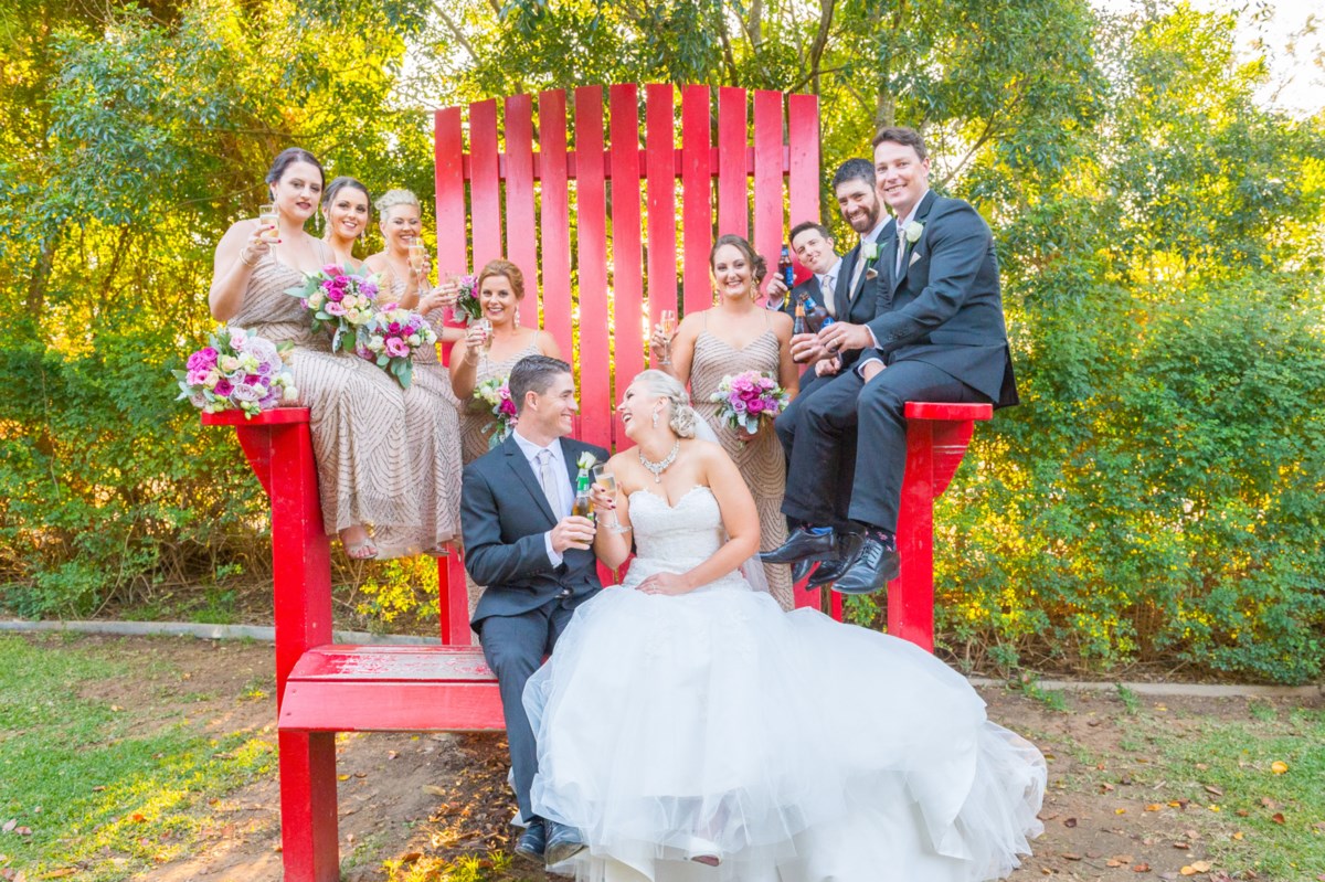 A bride, groom and their wedding party on the oversized big red chair in the Storybook Garden at Hunter Valley Gardens