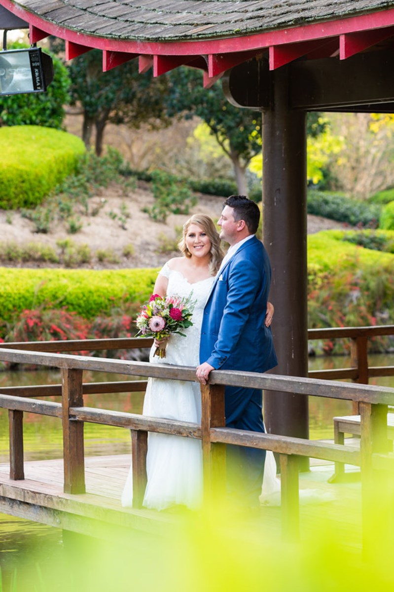 A couple on the deck over the pond at Hunter Valley Gardens, the red-beamed pagoda and manicured hedges behind them