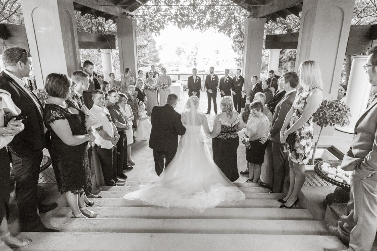 A bride walking down the stone steps toward a gazebo ceremony at Hunter Valley Gardens, guests seated either side