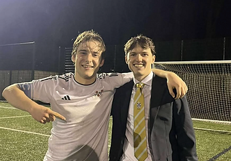Two NCAFC members on the pitch at night, with the club crest