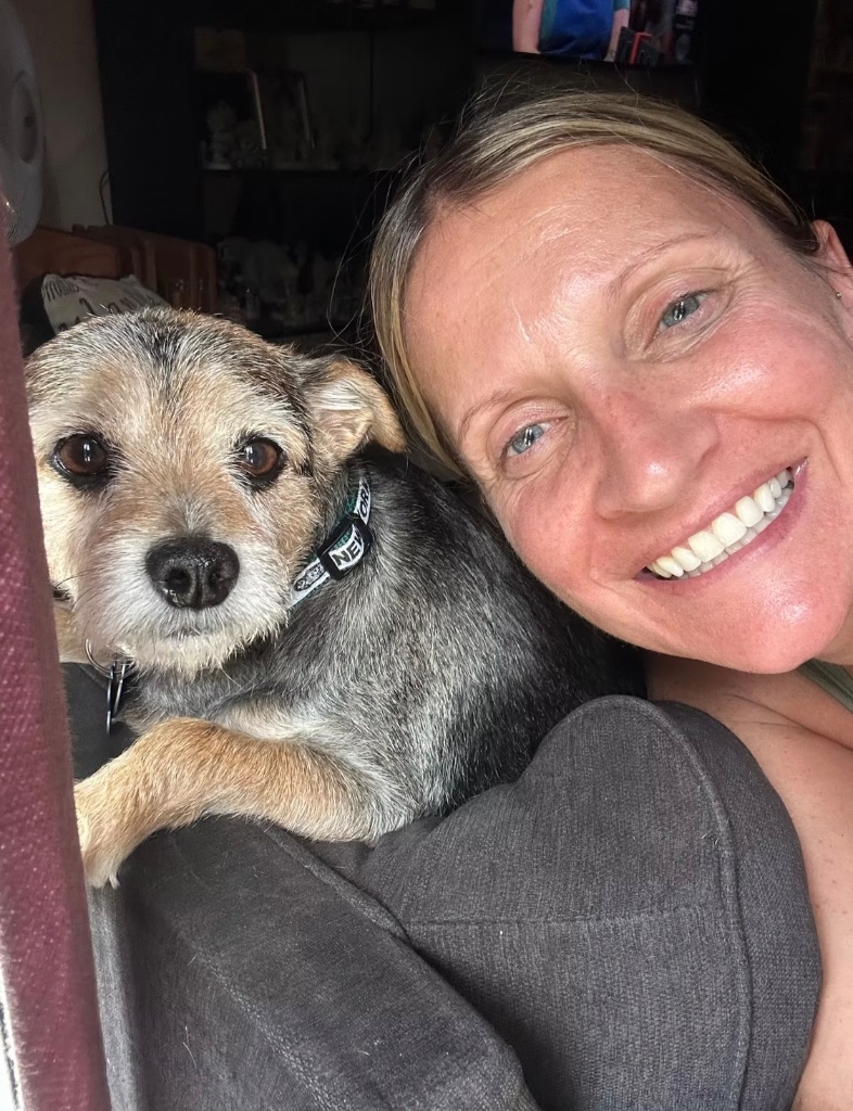 Casey smiling warmly while cuddling a small terrier mix dog