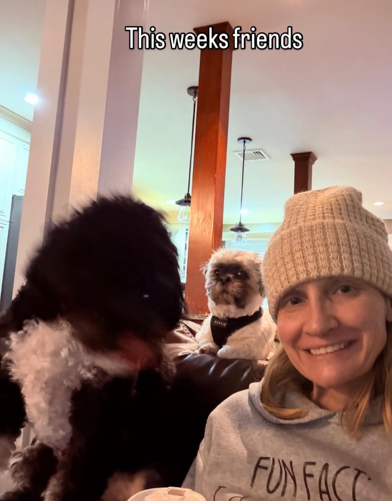 Casey smiling with two dogs — a fluffy black doodle and a small shih tzu in a bandana