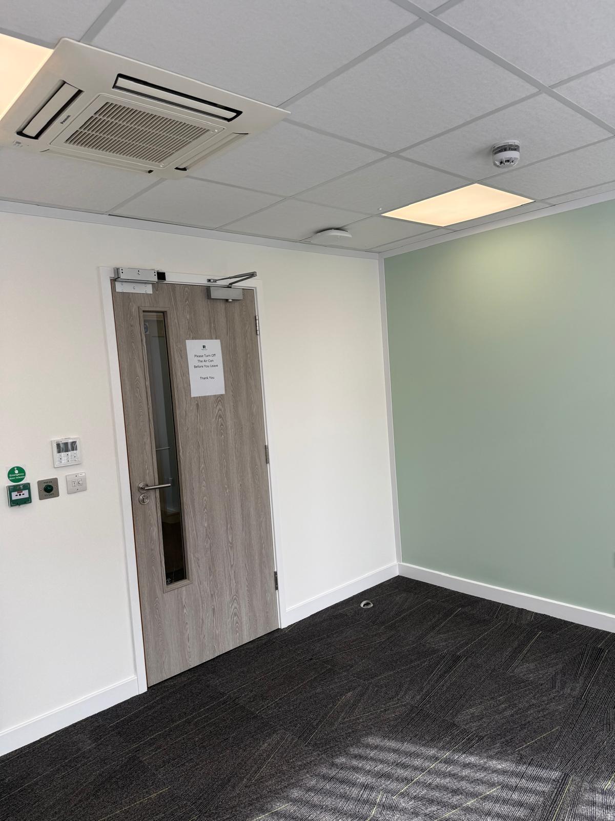 Clinic room door with air con reminder notice and Panasonic AC unit