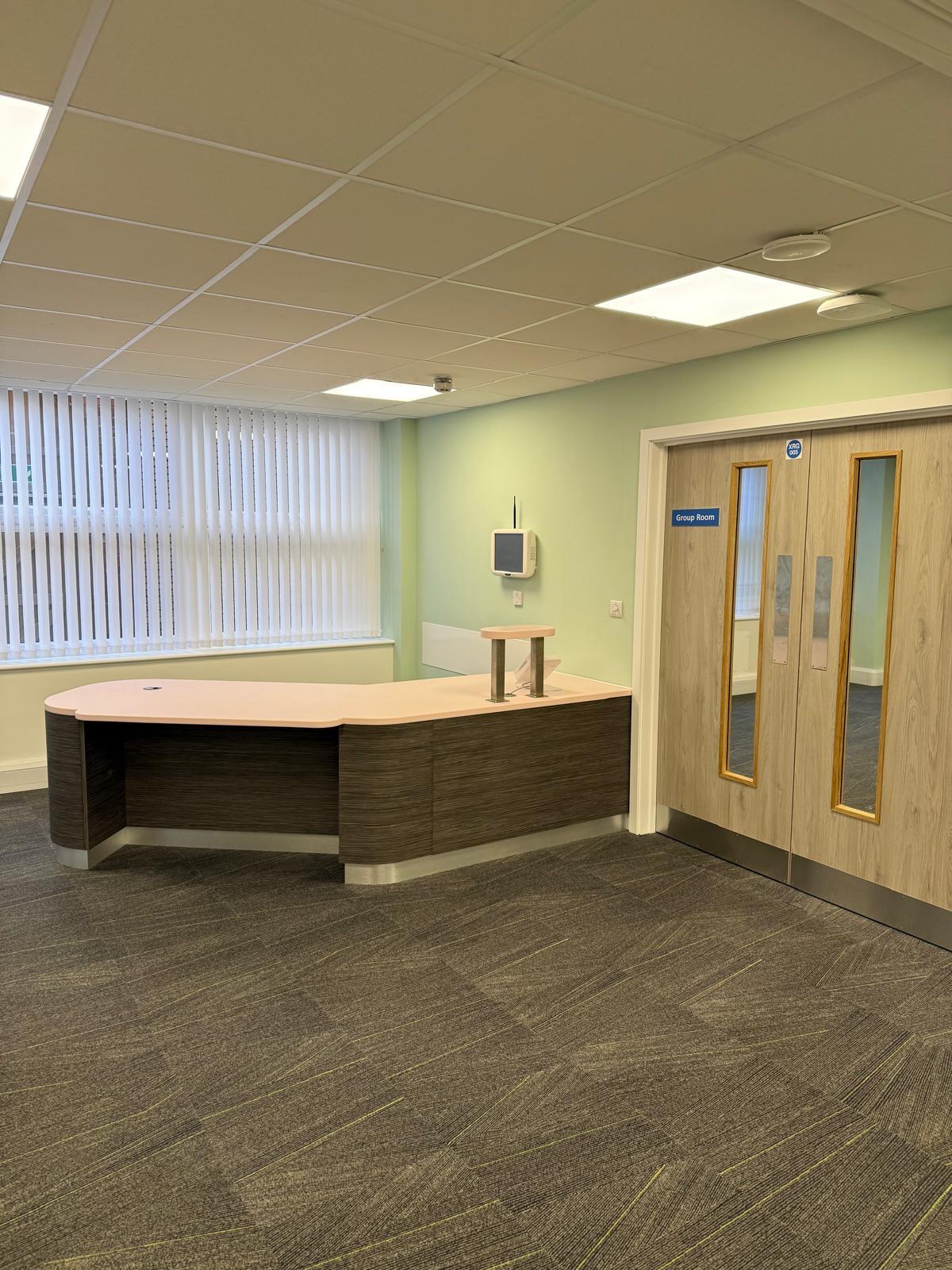 L-shaped reception desk with privacy screen and Group Room doors