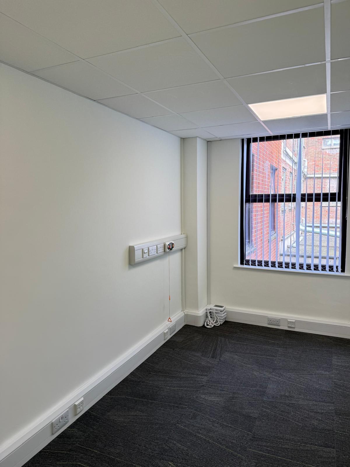 Office corner with emergency alarm pull-cord and window overlooking red brick buildings