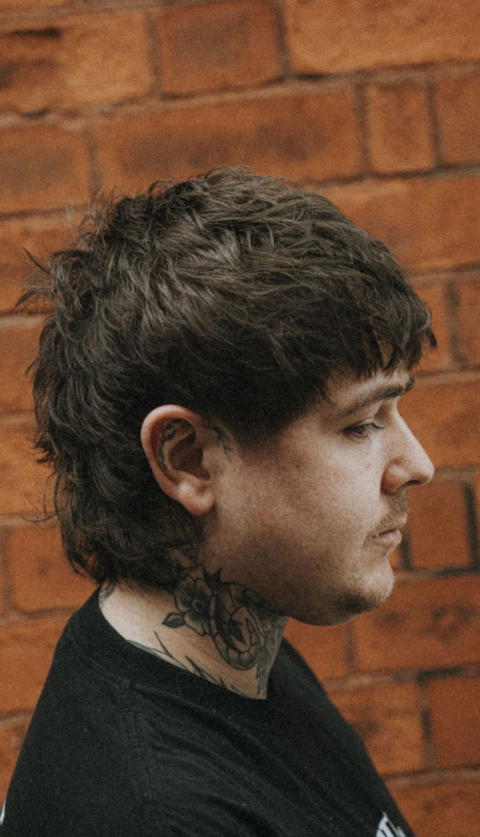 Profile portrait of a client with a textured mullet cut against a red brick wall