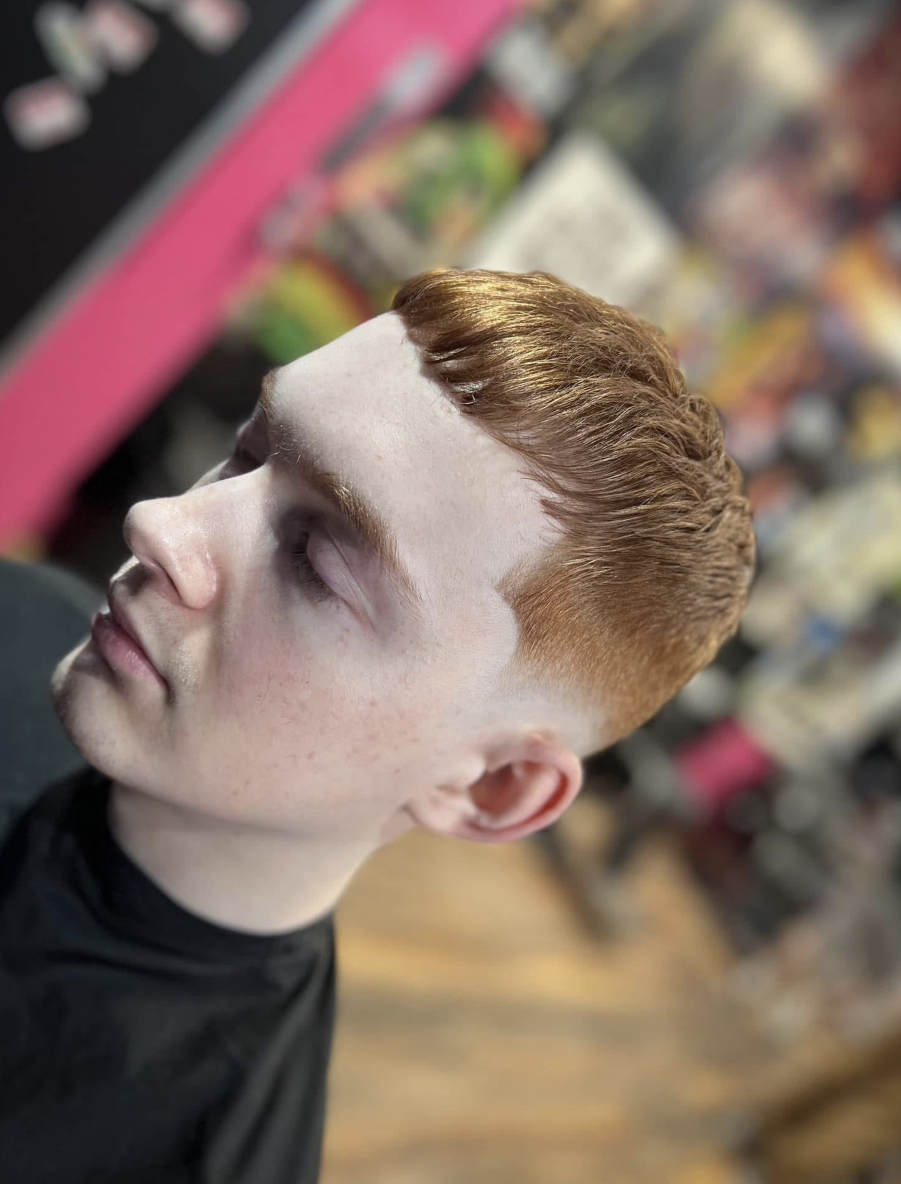 Side profile of a client with a light-brown textured fringe and skin fade