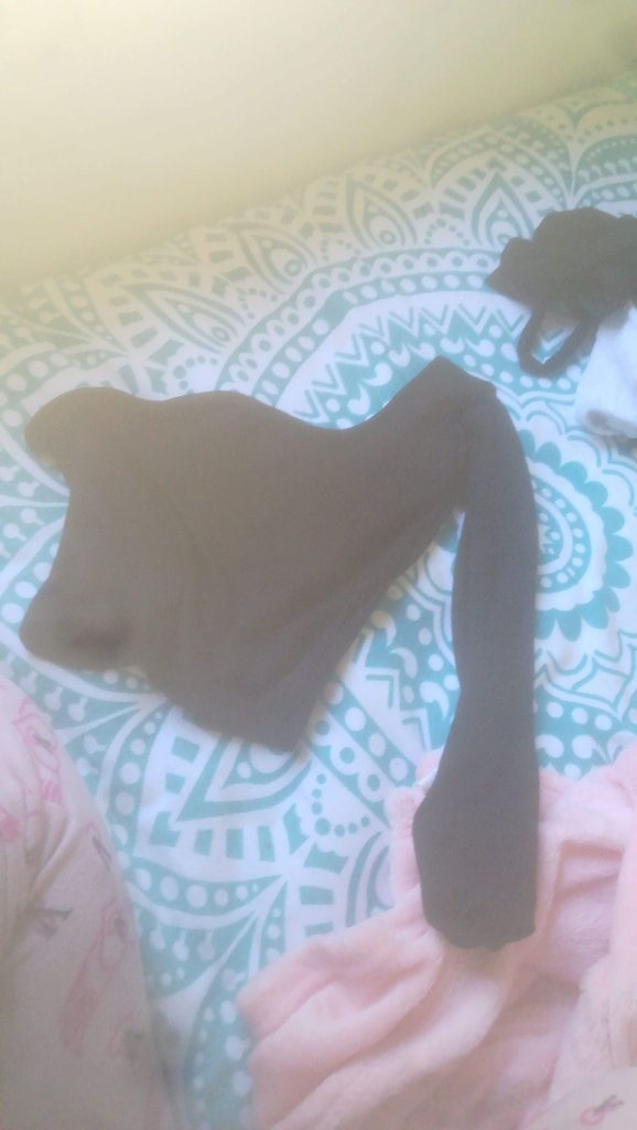 Prenda negra asimétrica con manga única sobre cama