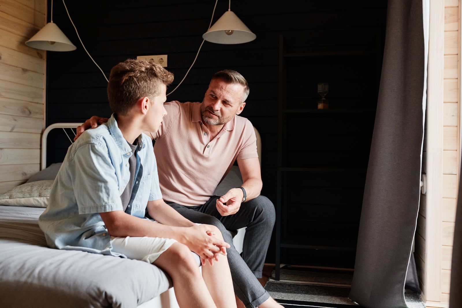 A father sitting beside his teenage son, talking calmly with a hand on his shoulder