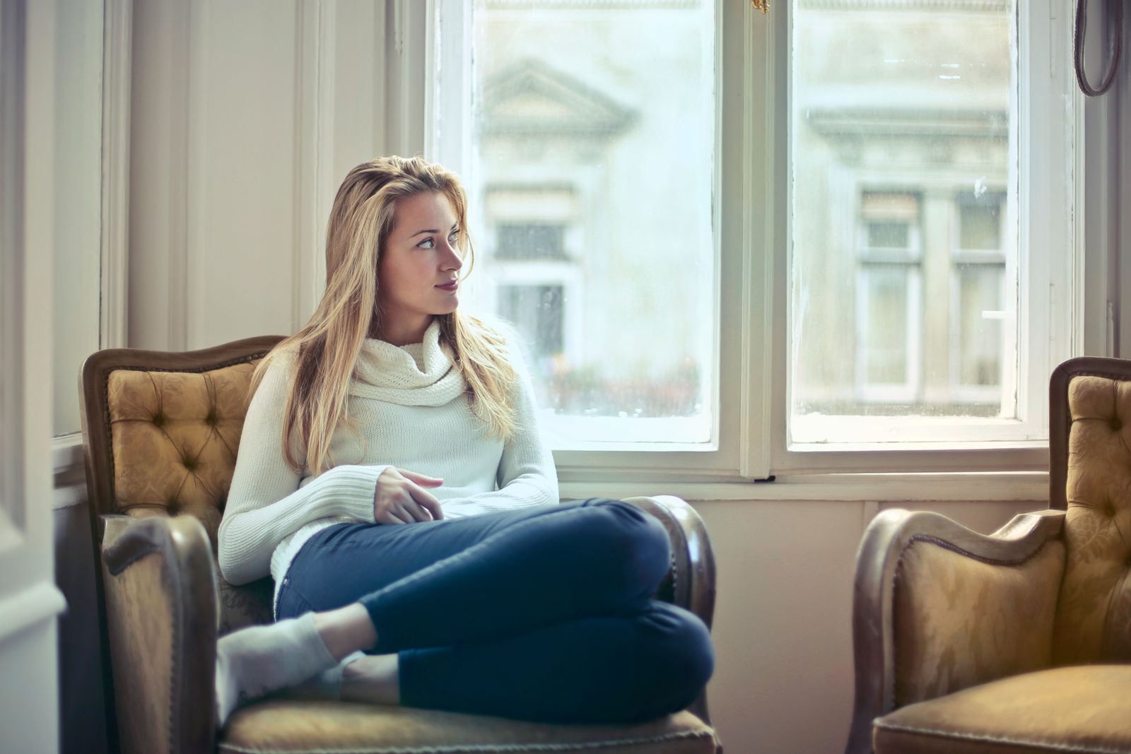 A woman sitting quietly in an armchair by a window, looking out