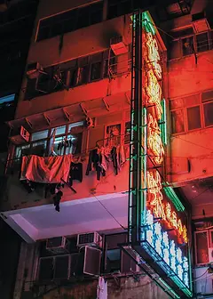 Nostalgia Card by ViewThroughJen'sLens - A nighttime image of a building with vibrant neon signage, where laundry flutters from the balconies, capturing the essence of city life