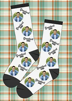 Greatest Dad white socks with black heels and cuffs on a green and orange plaid background, perfect for a Christmas gift.