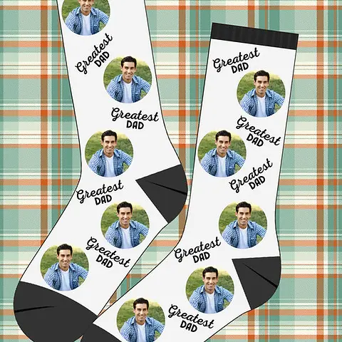 Greatest Dad white socks with black heels and cuffs on a green and orange plaid background, perfect for a Christmas gift.