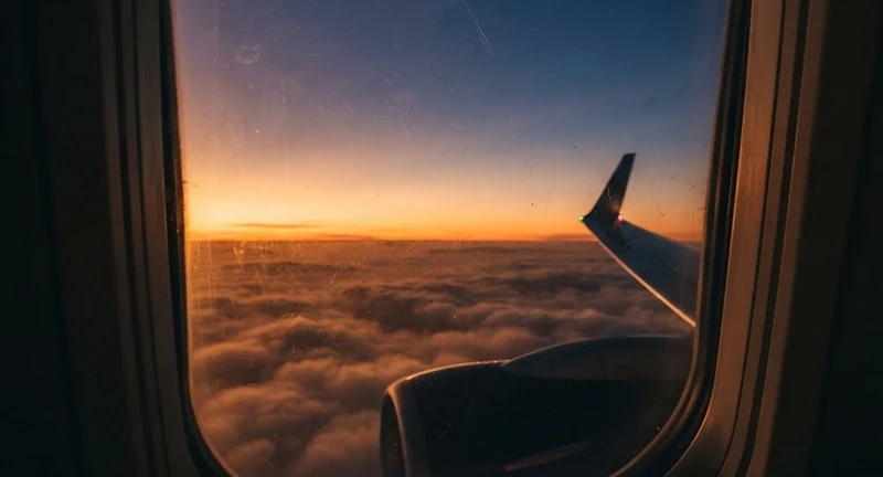 Airplane window at dusk with a warm amber horizon fading into indigo twilight