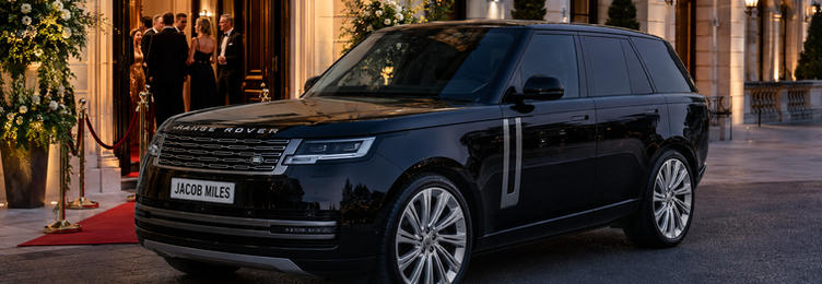 Black Range Rover chauffeur vehicle parked outside an elegant event venue with red carpet entrance at dusk