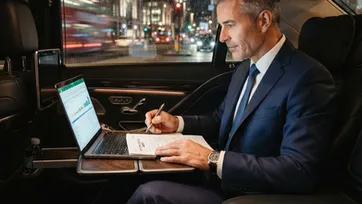 Business executive working on a laptop in the back of a luxury chauffeur vehicle for a London roadshow