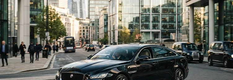 Black executive saloon on a city street with modern glass office buildings in bright natural daylight
