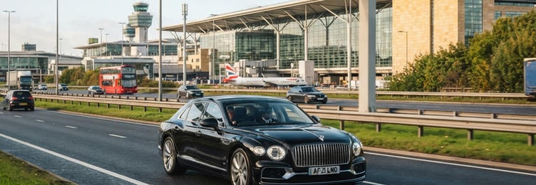 Black executive saloon on a highway with airport terminal signage in the distance in bright natural daylight