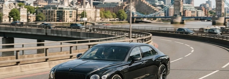 Black executive saloon on an urban flyover with the London city skyline behind in bright natural daylight
