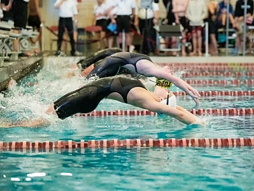 Two swimmers launching backstroke starts over the lanes of an indoor competition pool