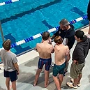 A coach talking with young swimmers at the pool edge