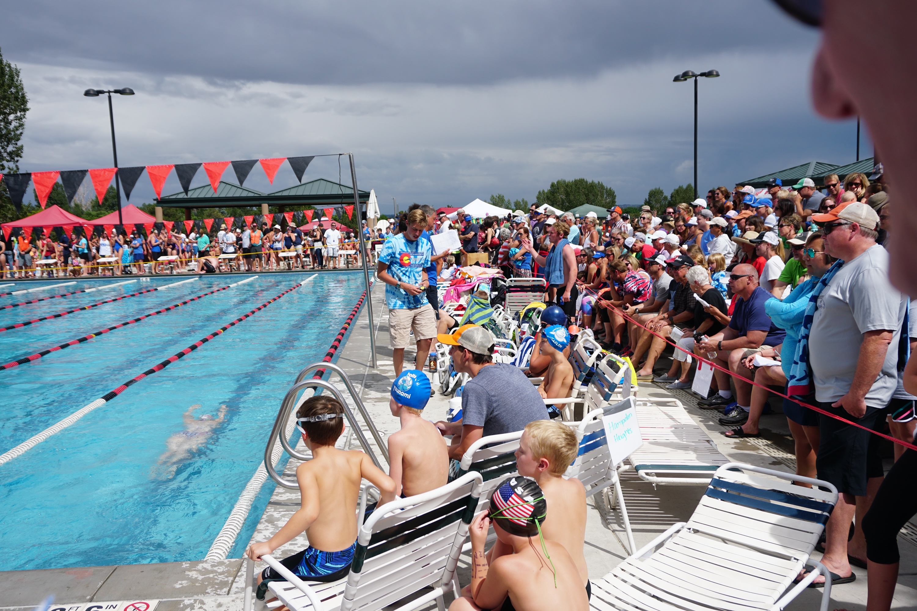 A crowded outdoor pool deck packed with swimmers, families and spectators during a swim meet