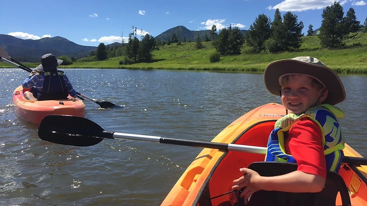 A young paddler wearing a life vest in a kayak on a mountain lake