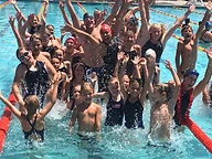 A crowd of young swimmers cheering with arms raised in the pool