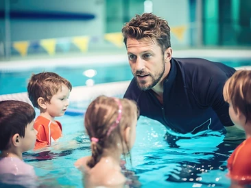 Swim instructor leaning in to talk with young children during an indoor swim lesson